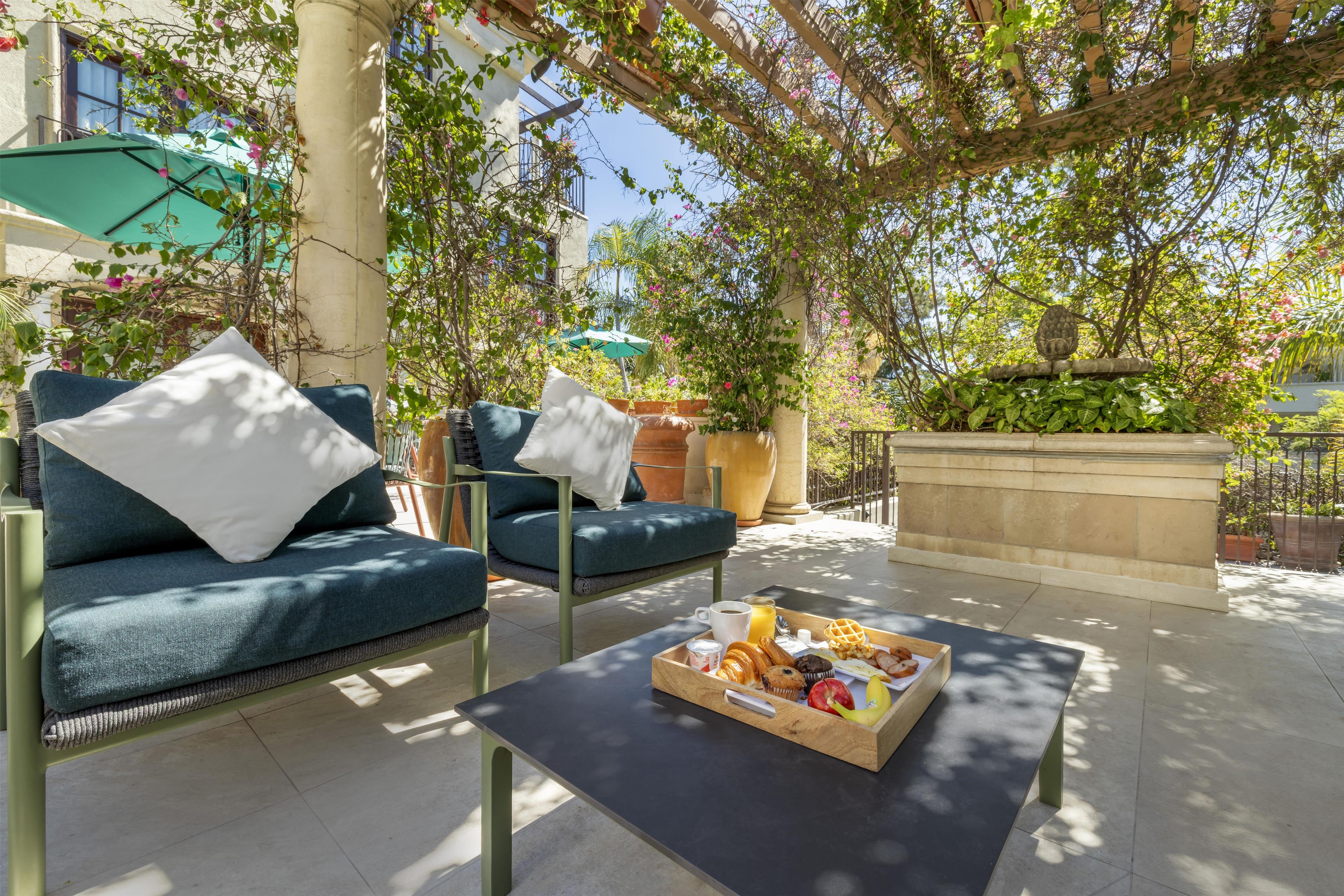 An outdoor seating area with a sofa, a table with a tray of food, and a pergola with climbing plants.