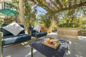 Un espace extérieur aménagé avec un canapé, une table sur laquelle est disposé un plateau de nourriture et une pergola couverte de plantes grimpantes.