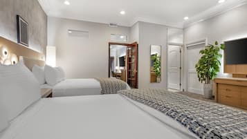 Quarto de hotel com duas camas, uma escrivaninha, um espelho, uma televisão e uma planta.