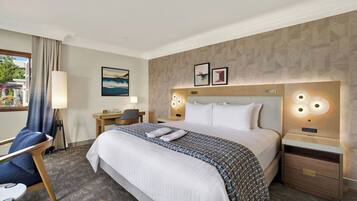 Habitación de hotel con una cama grande, mesitas de noche, un escritorio, una silla y vistas al exterior.