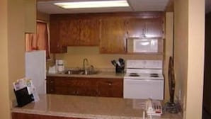 A compact kitchen with wooden cabinets, a white stove, and a microwave. - Sunset Inn & Suites - Lincoln Airport (Lincoln)