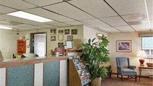 A reception area with a counter, a plant, a chair, and a wall with framed pictures. - Sunset Inn & Suites - Lincoln Airport (Lincoln)