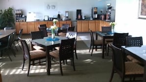 A spacious dining area with multiple tables and chairs, a kitchen in the background, and a ceiling with recessed lighting. - Sunset Inn & Suites - Lincoln Airport (Lincoln)