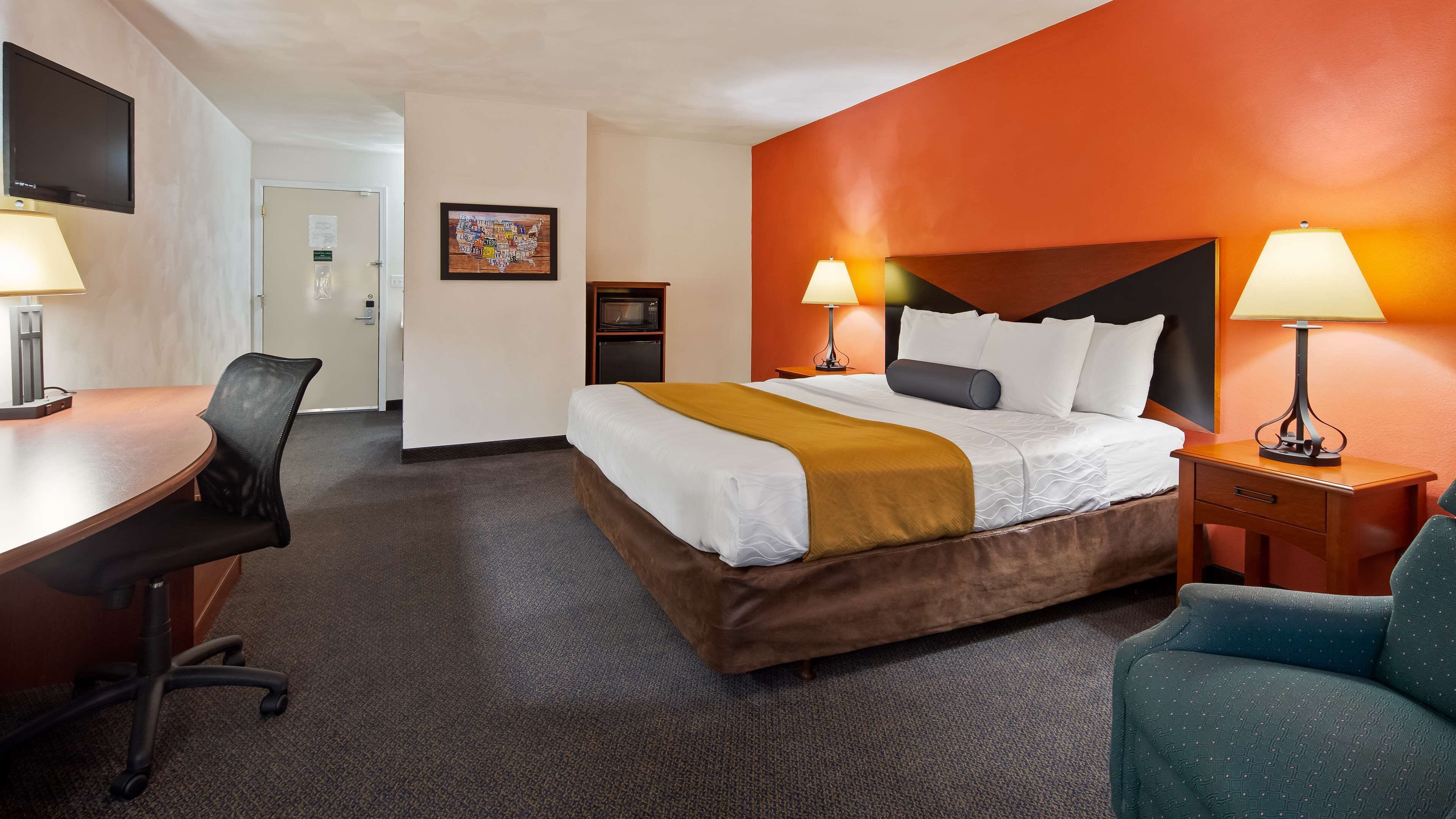 A hotel room with a bed, desk, chair, and two lamps.