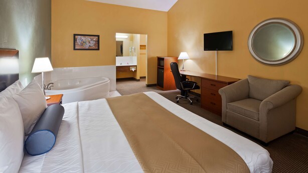A hotel room with a large bed, a desk, a chair, a TV, a mirror, and a bathroom with a bathtub and sink.