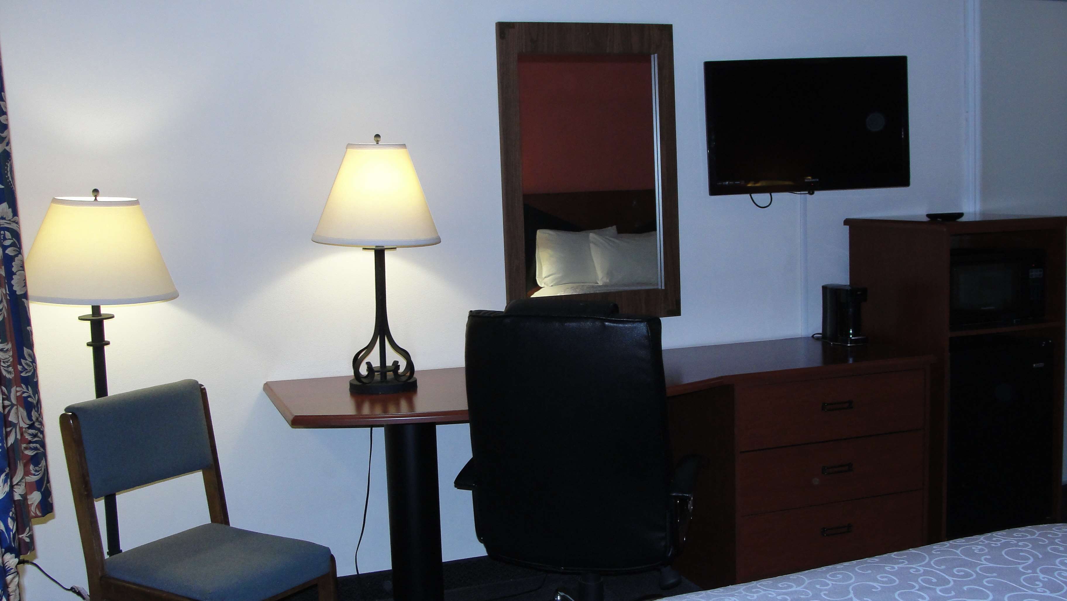 Ett hotellrum med ett skrivbord, två lampor, en stol, en byrå, en tv och en säng.