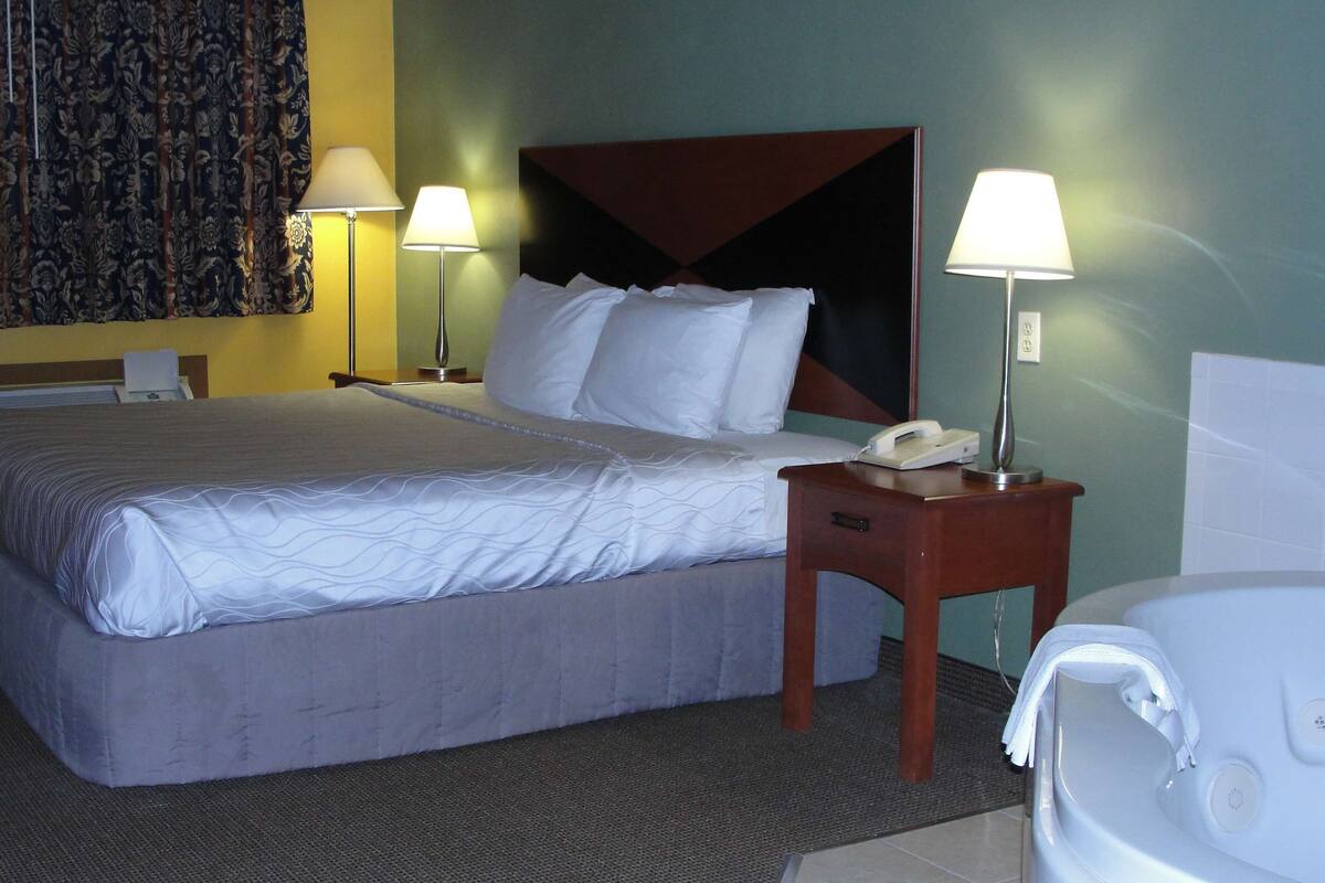 A hotel room with a large bed, two bedside lamps, a bedside telephone, and a bathroom with a white bathtub.