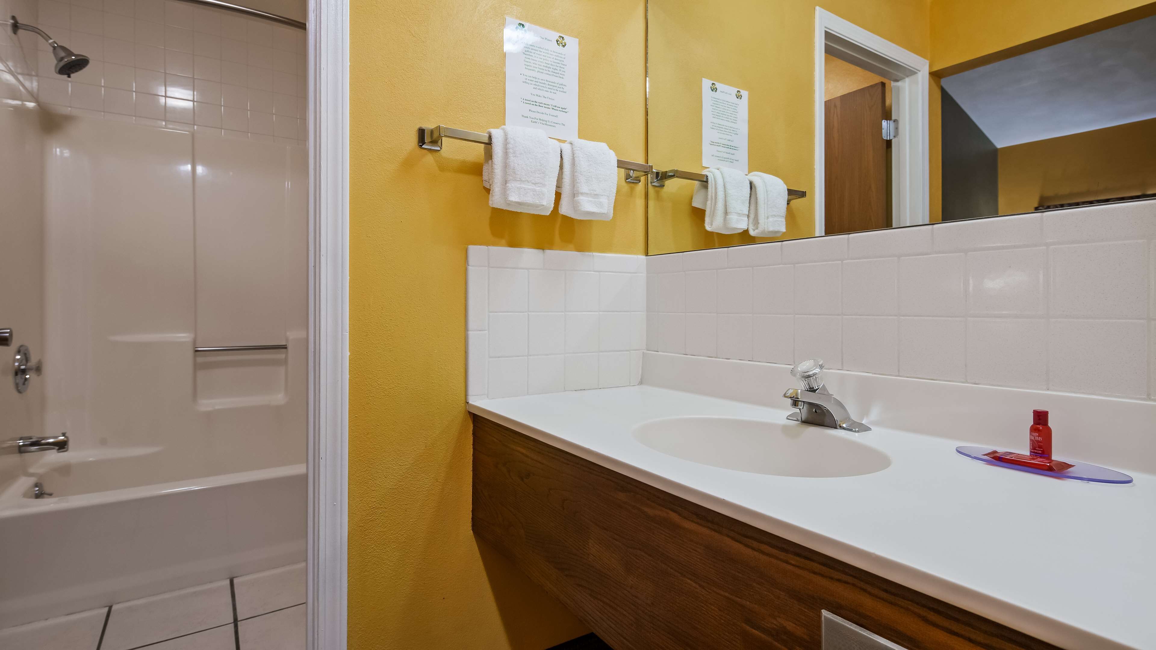 A bathroom with a white bathtub, a wooden vanity with a sink, and a mirror. There are towels hanging on a rack and a showerhead above the bathtub.