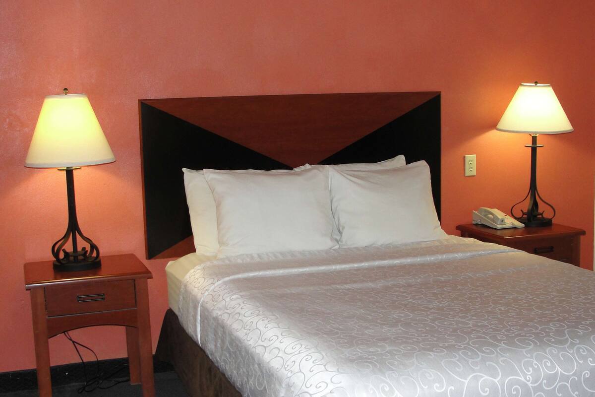 A hotel room with a bed, two bedside tables with lamps, a telephone, and a power outlet on the wall.