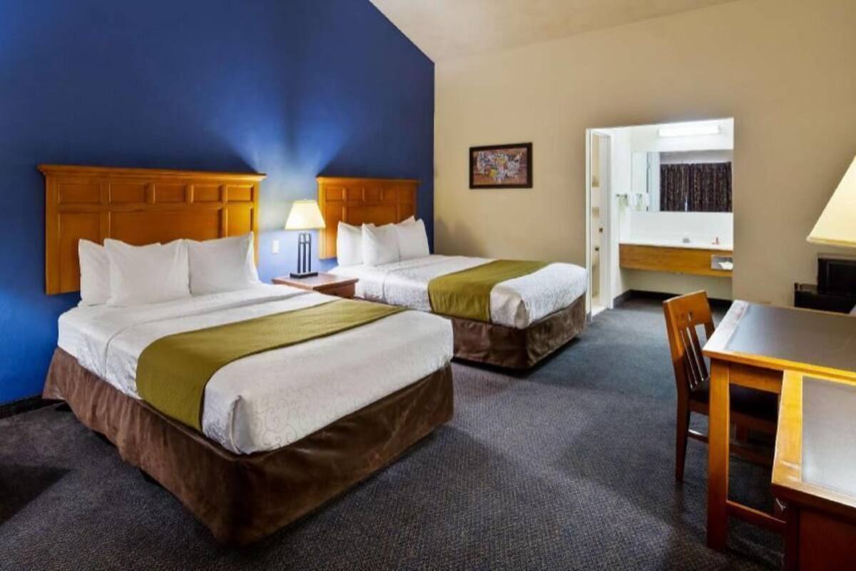 A hotel room with two beds, a desk, a chair, and a bathroom visible through an open door.