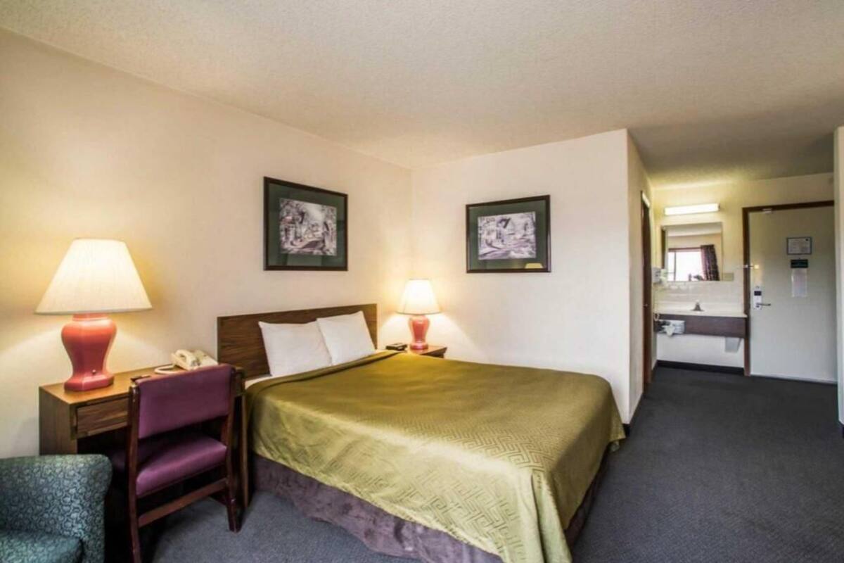 A hotel room with a bed, two bedside lamps, a chair, and two framed pictures on the wall.