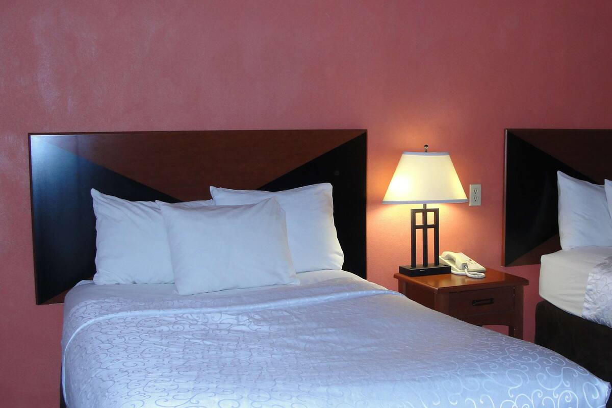 Two single beds with white linens and headboards, a bedside table with a lamp, and a telephone.