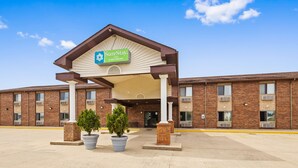 A SureStay hotel entrance with a covered waiting area, brick facade, and potted plants.