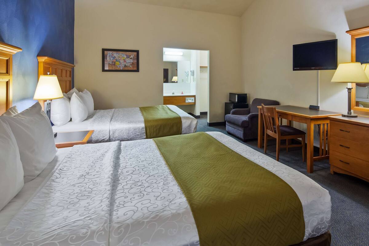 A hotel room with two beds, a desk, a chair, a dresser, a TV, and a mirror.