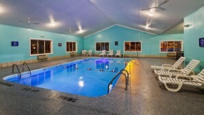 An indoor swimming pool with clear water, surrounded by lounge chairs and a ceiling fan.