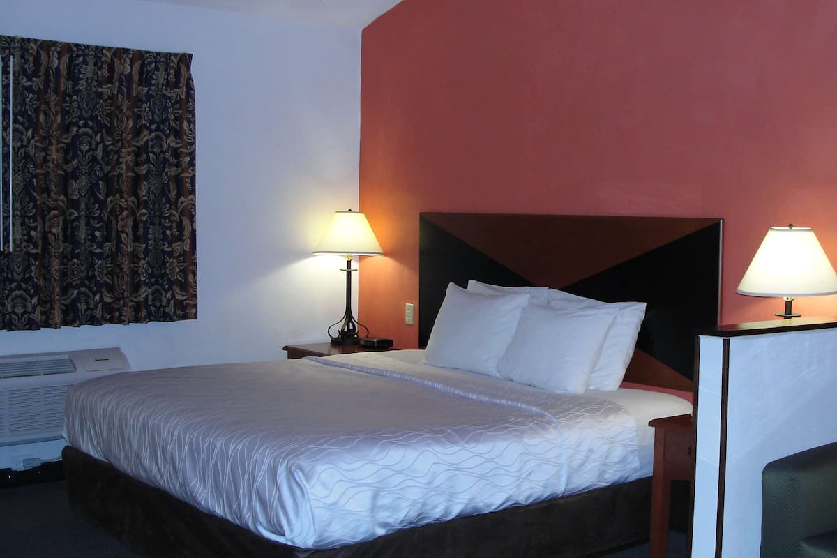 A hotel room with a bed, two bedside lamps, a nightstand, a chair, and a window with curtains.