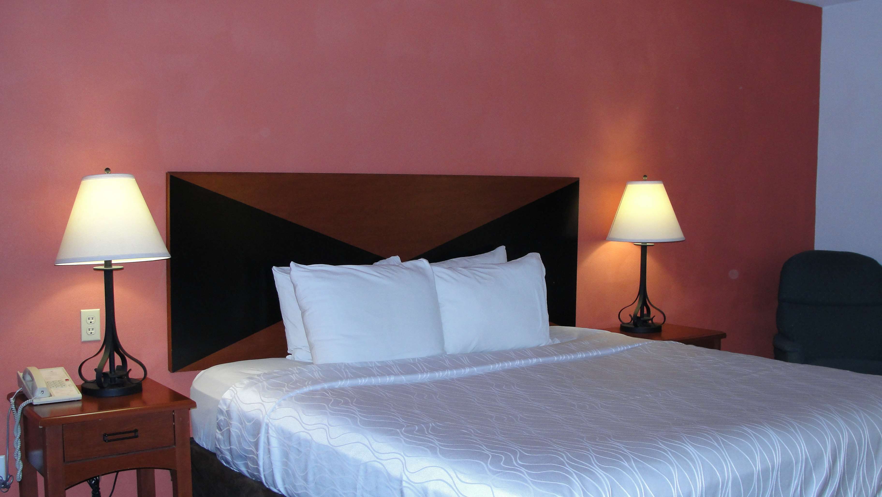 A hotel room with a large bed, two bedside lamps, a telephone, and a chair.