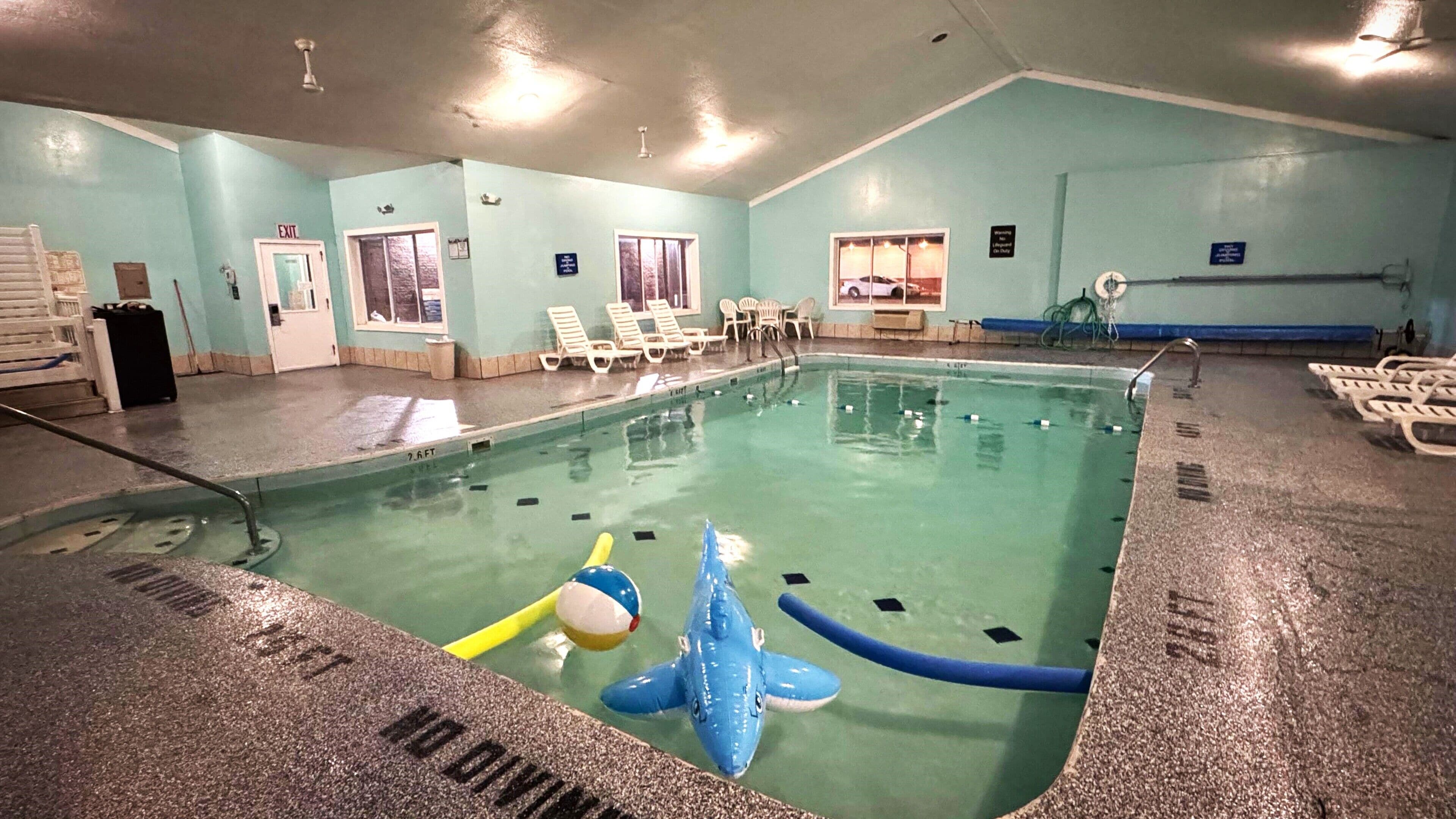Une piscine intérieure avec un flotteur en forme de requin bleu, des chaises longues et un poste de surveillance pour les sauveteurs.
