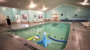 An indoor swimming pool with a blue shark float, lounge chairs, and a lifeguard stand.