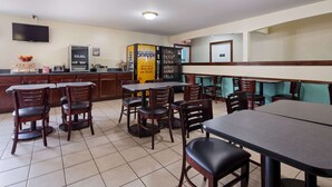 A restaurant with wooden tables and chairs, a kitchen area, and a vending machine.