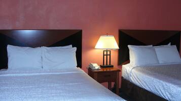 A hotel room with two beds, a nightstand with a lamp, and a phone.