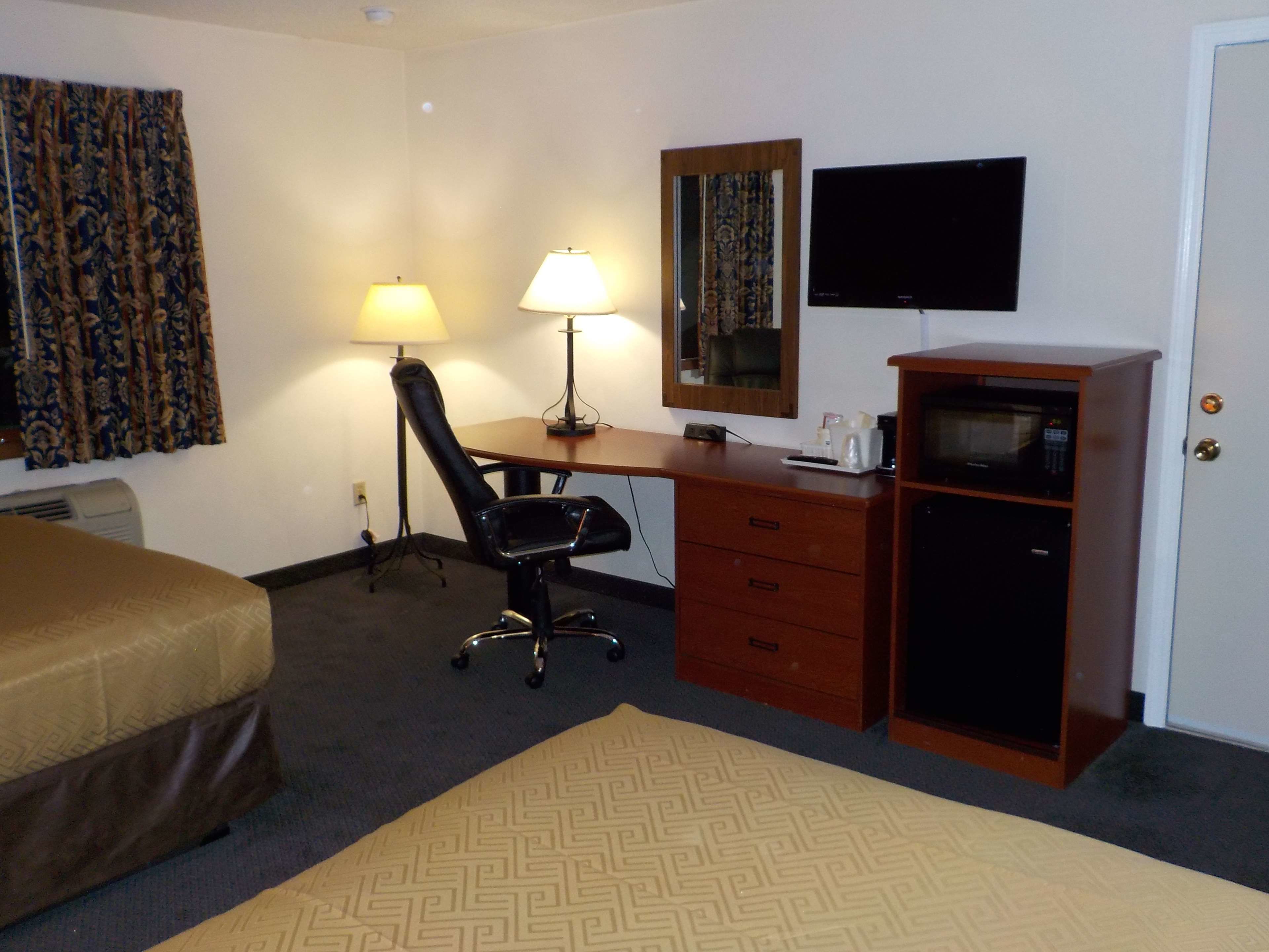 Une chambre d’hôtel équipée d’un lit, d’un bureau, d’une chaise, d’une commode, d’une télévision et d’un four à micro-ondes.
