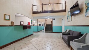 A hotel lobby with a reception desk, a staircase to an upper level, a sofa, and a TV mounted on the wall.