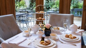 A table set for a tea service with a tiered tray, teapot, cups, saucers, and a vase with flowers.