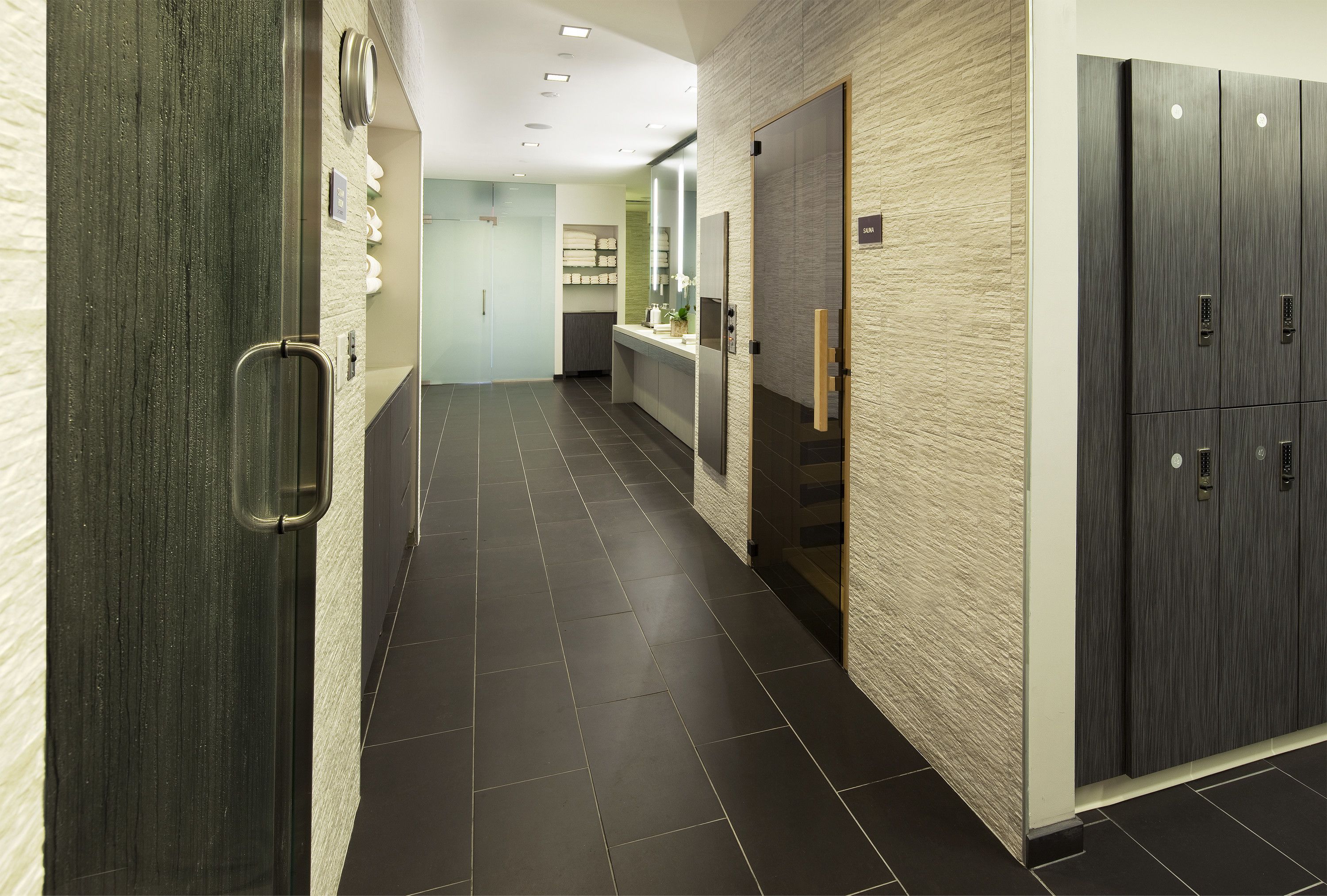 A modern hallway with a dark tiled floor, a wooden door on the left, a mirror on the right, and a wardrobe with a light-colored textured wall.