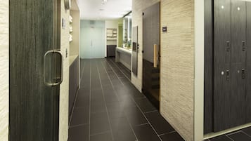 A modern hallway with a dark tiled floor, a wooden door on the left, a mirror on the right, and a wardrobe with a light-colored textured wall.