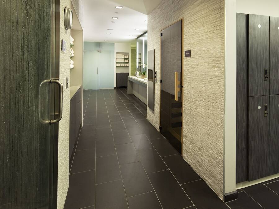 A modern hallway with a dark tiled floor, a wooden door on the left, a mirror on the right, and a wardrobe with a light-colored textured wall.