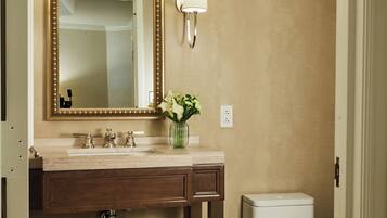 Un baño con pared color beige, un espejo grande, un lavamanos con un florero y un inodoro, además de un mueble de tocador de madera.