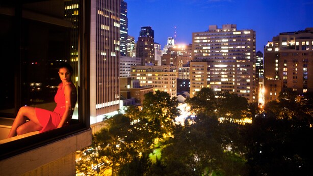 A cityscape at night with illuminated buildings and a person sitting by a window.