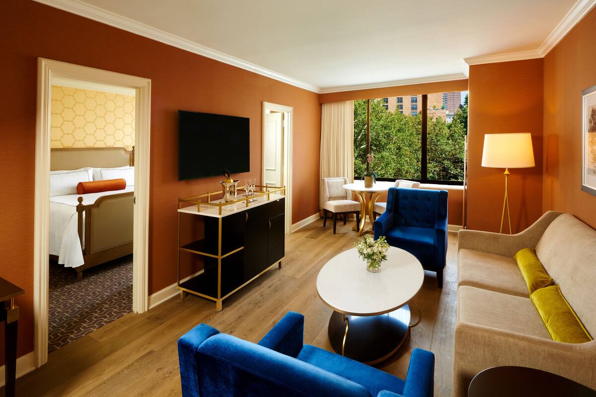 A hotel room with a bed, a desk, a blue sofa, a round coffee table, and a TV.