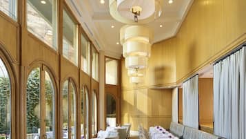 Un restaurante con mesas largas, sillas elegantes y amplias ventanas.
