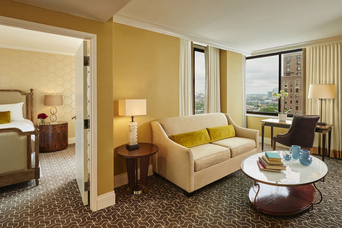 A hotel room with a bed, a sofa, a round coffee table, and a view of the city.
