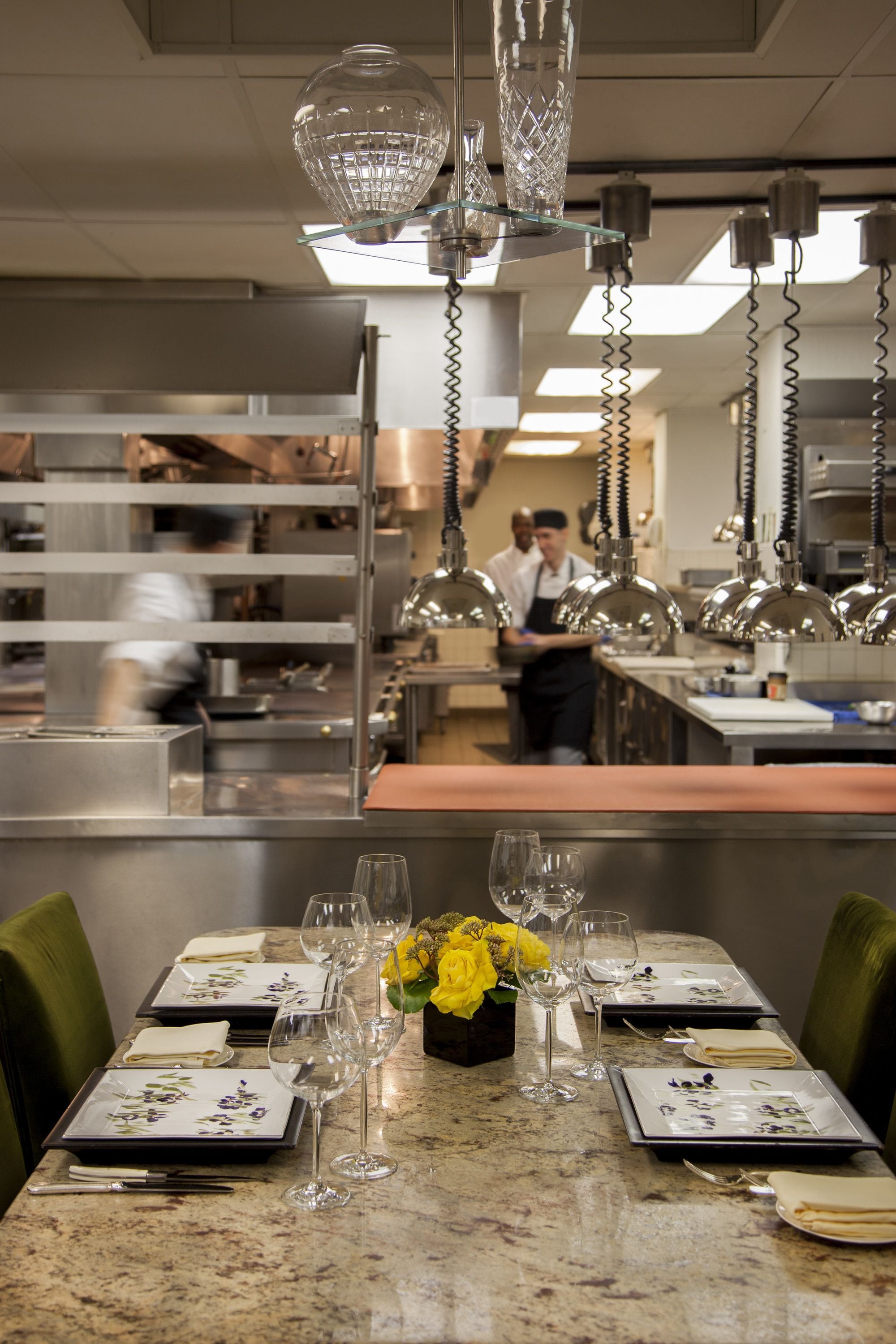 A restaurant setting with a marble table set for dining, featuring plates, glasses, and a vase of yellow flowers.