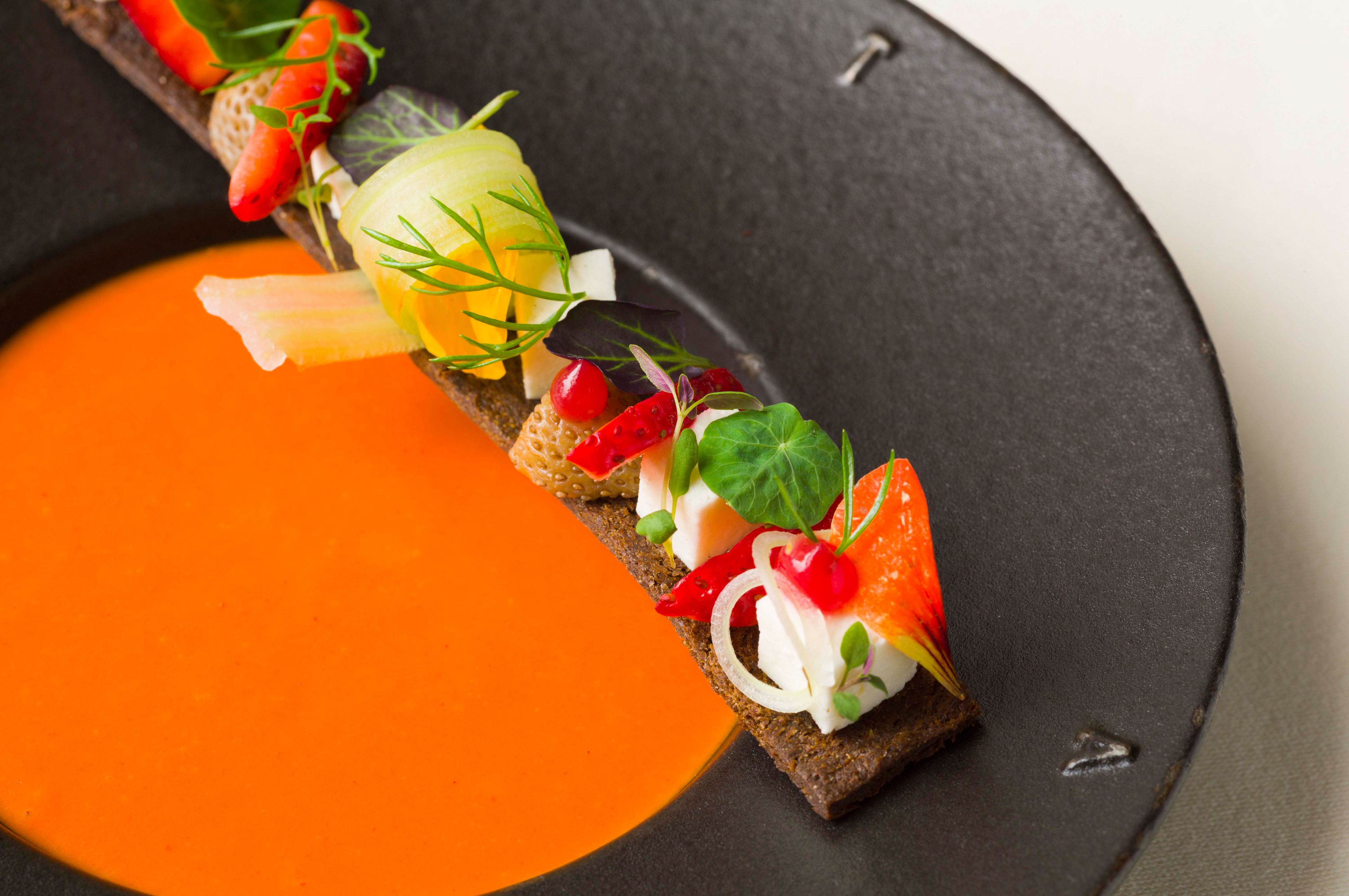 A dish with various toppings on a slice of bread, accompanied by a side of orange sauce.