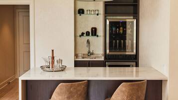 A modern kitchen with a central island, two bar stools, a built-in wine cooler, and a stainless steel refrigerator.