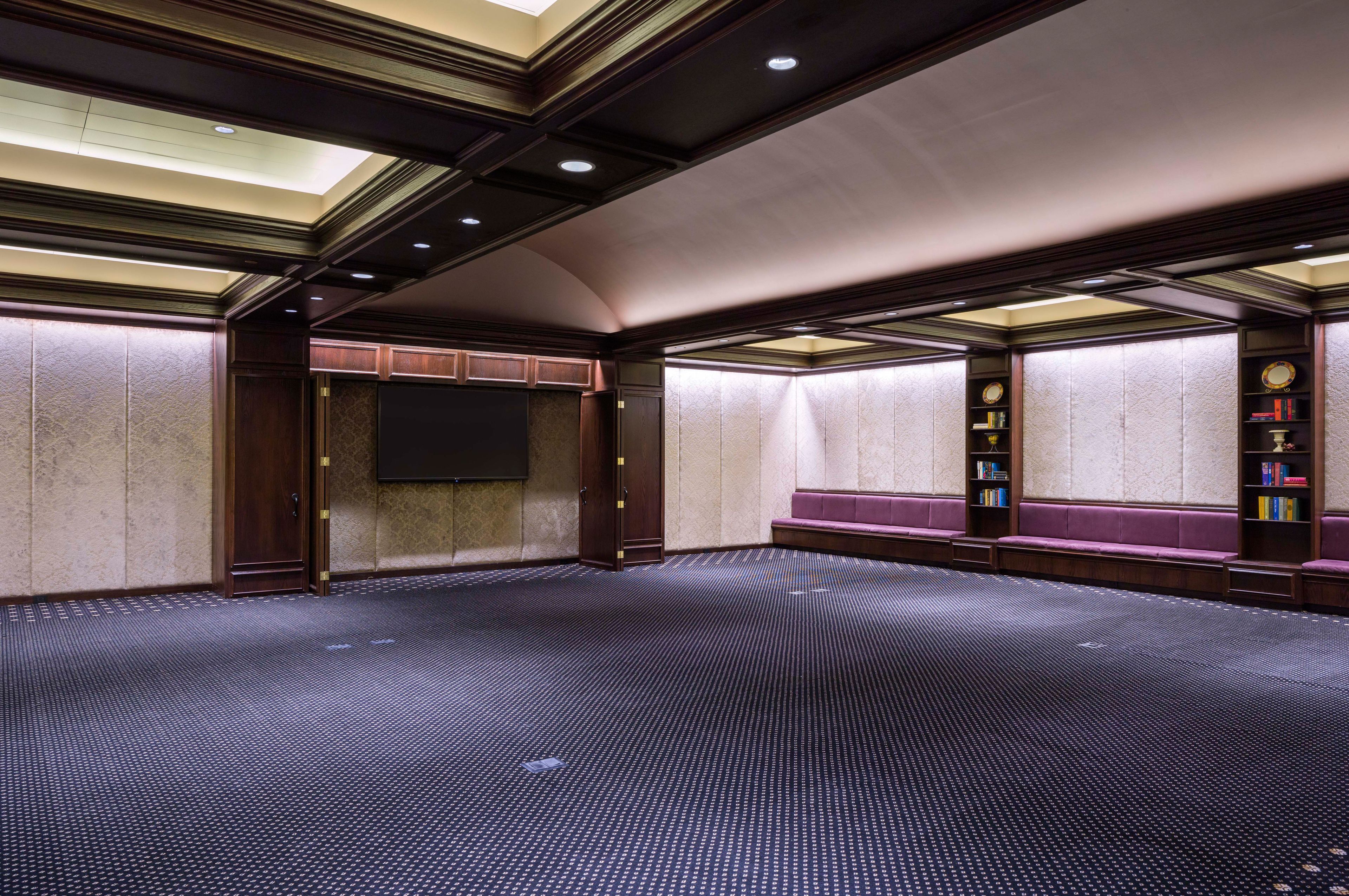 A conference room with a large screen, wooden paneling, and a carpeted floor.
