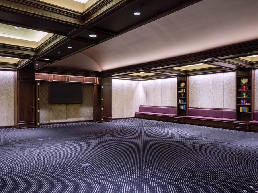 A conference room with a large screen, wooden paneling, and a carpeted floor.
