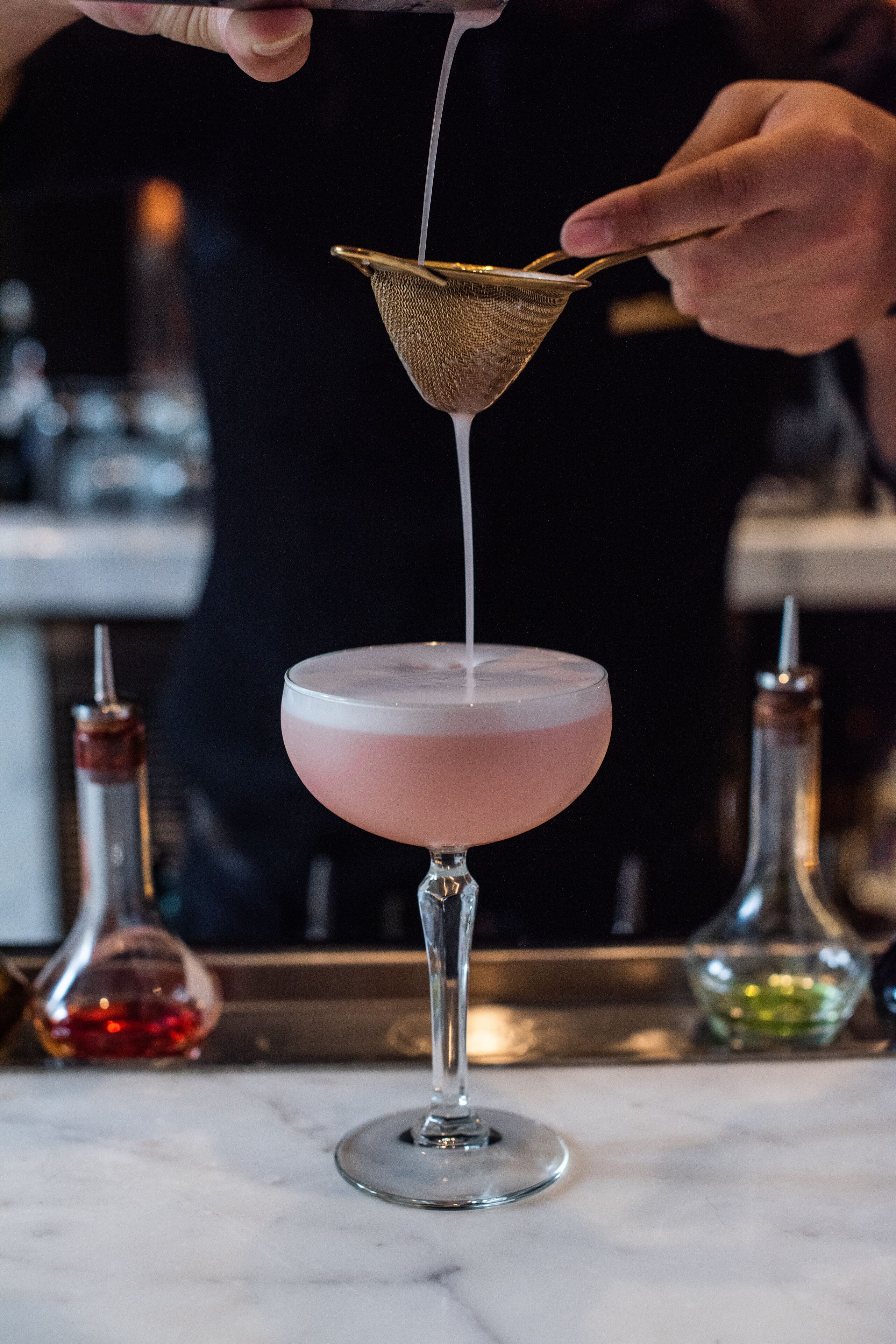 Ein Barkeeper gießt ein Getränk in ein pinkes Cocktailglas.
