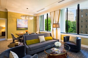 Una habitación de hotel moderna con sofá, sillones, una mesa de comedor y un ventanal con vistas a la ciudad.