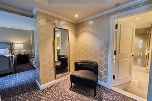 A hotel room with a patterned carpet, a large mirror, a tufted armchair, and a door leading to a bathroom. - The Rittenhouse Philadelphia (Philadelphia)