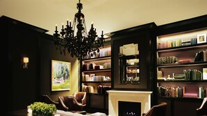 A dark-themed library with a fireplace, bookshelves, and leather chairs.