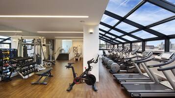 Une salle de sport moderne équipée de machines de cardio, de poids et d’une grande baie vitrée donnant sur la ville.