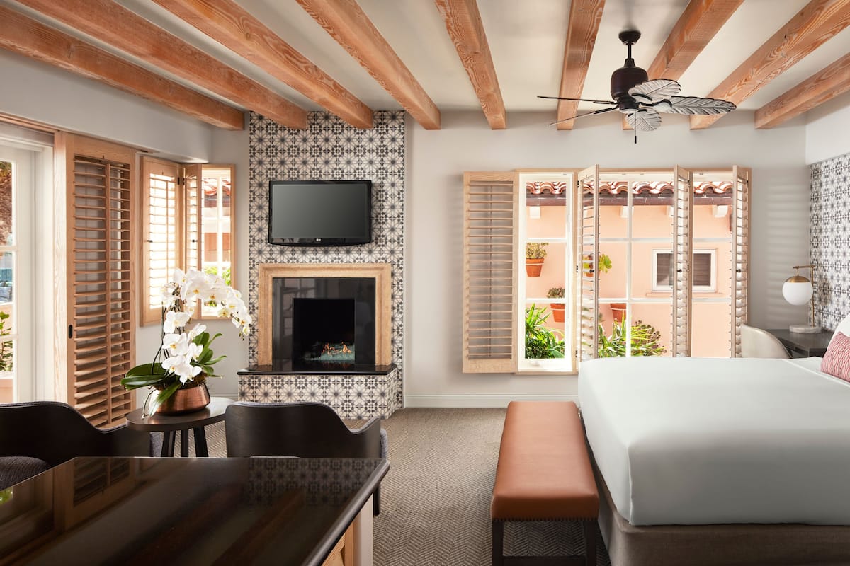 A hotel room with a fireplace, a bed, a dining area, and a view of the outside balcony.