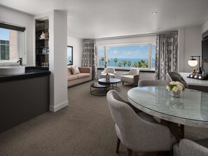 A modern living room with a sofa, chairs, a glass table, and a view of the ocean.