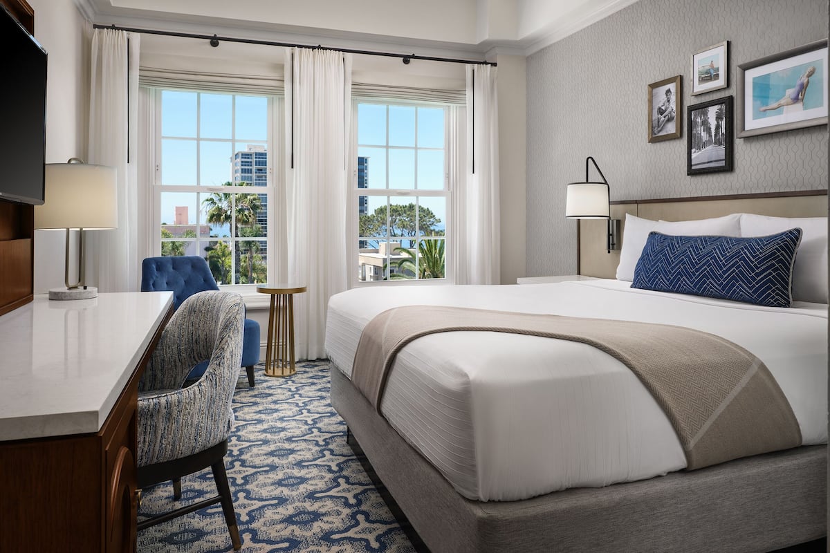 A hotel room with a bed, a desk, a chair, and a view of the city.