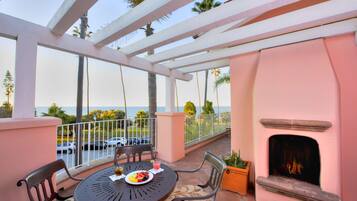 A balcony with a table, chairs, a fire pit, and a view of the ocean.